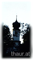 Kirchturm als Silhouette zwischen Bäumen