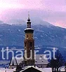 Kirchturm und Dächer vor einer verschneiten Landschaft